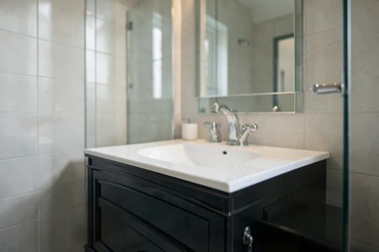 Um banheiro elegante com azulejos claros, box de vidro e bancada com cuba.